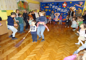 Dzieci i rodzice wspólnie tańczą. W środku dzieci z mamą tańczą z miotłą.